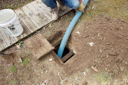 a septic system service technician holds a pump hose coming from a whole in the ground